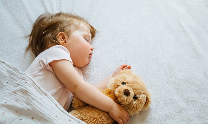 bebê dormindo na cama com bichinho de pelúcia - filho dorme mal